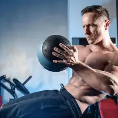 Homme musclé effectuant un exercice oblique avec un medecine ball, concentré sur son entraînement.