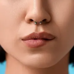Kobieta z septum w nosie i kolczykami w uszach na niebieskim tle.