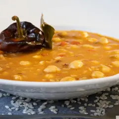 Un plato de garbanzos con arroz, con un pimiento seco y una hoja de laurel encima.