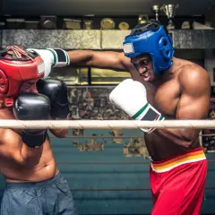 Två boxare i ringen, en med röd och en med blå hjälm, tränar funktionell fitness.