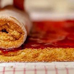 Un rouleau de génoise moelleuse, saupoudré de sucre glace, est en train de rouler sur une couche de confiture de fraises éclatante.