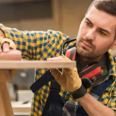 Artisan méticuleux, il s'applique à raboter une porte en bois avec soin.