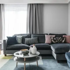 Szara kanapa z kolorowymi poduszkami i geometrycznym dywanem.