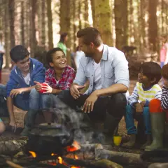 Kinder lachen und trinken am Lagerfeuer. Ein Lehrer verweigert die Klassenfahrt, aber die Kinder genießen den Ausflug trotzdem.