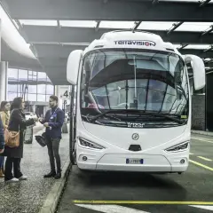 Autobus Terravision czeka na pasażerów na jednym z mediolan lotniska. Ludzie z bagażami rozmawiają z pracownikiem.