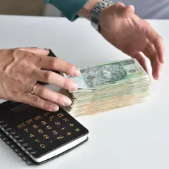 Ręce liczą stos banknotów, obok kalkulator. Jak odzyskać pieniądze z banku po zmarłej osobie?