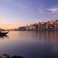 Barcos tradicionales navegan por el río Duero al amanecer, con la pintoresca ciudad de Oporto al fondo. Un lugar imprescindible que ver en el norte de Portugal.