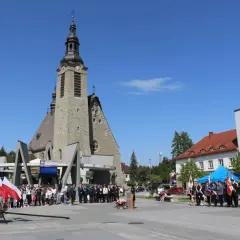 Uroczystość przed kościołem w Limanowej. Ludzie, delegacje w mundurach i polskie flagi.