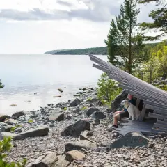 En man och hans hund njuter av en lugn semester vid vattnet, omgivna av stenar och träd.
