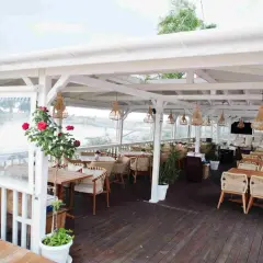 Letnia restauracja z widokiem na wodę. Krzesła i stoły z rattanu, wiszące lampy. Idealne miejsce na pyszne jurata jedzenie.