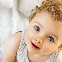Uśmiechnięte niemowlę z niebieskimi oczami i kręconymi blond włosami na białym tle.