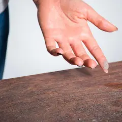Mano con polvo en los dedos sobre una mesa de madera, indicando la necesidad de limpiar el polvo.