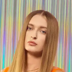 Sophie, top model o długich, blond włosach, pozuje na tle błyszczącej, tęczowej kurtyny.