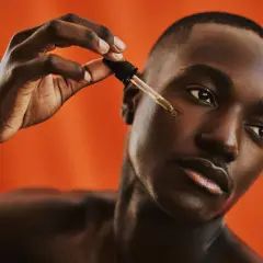 Uomo con pelle scura applica un siero con contagocce, parte della sua beauty routine viso.