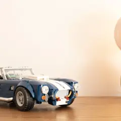 Ein blauer Lego Shelby Cobra steht neben einer leuchtenden Glühbirne.