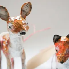 Urocze figurki z papier mache: jelonek w plamki i lis. Ich uszy zdobią fragmenty tekstu.