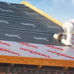 Ocieplenie dachu od zewnątrz. Pracownik montuje izolację THERMANO na konstrukcji dachu.
