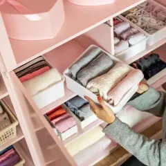 Frau sortiert Kleidung in einem rosa Kleiderschrank. So organisiere ich meinen Kleiderschrank: gefaltete Pullover und Socken in Behältern.