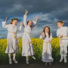 Cztery dzieci w strojach komunijnych skaczą na tle kwitnącego pola rzepaku.