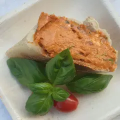 Ein Stück Brot mit leckerer Tomatenbutter, garniert mit frischem Basilikum und einer Kirschtomate. Perfekt zum Tomatenbutter selber machen.