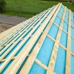 Drewniana konstrukcja dachu z widocznym niebieskim materiałem izolacyjnym. Styropian między krokwie zapewnia ciepło.