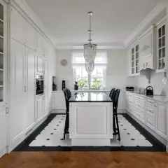 Elegancka, biała kuchnia półotwarta na salon z wyspą i czarnymi hokerami. Luksusowy żyrandol dodaje blasku.