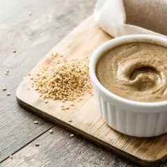 Domowe tahini jak zrobić? Ziarna sezamu i gotowa pasta na desce.