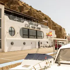 Edificio blanco con el letrero "C.N. SAN JOSE" y una bandera española ondeando. Un restaurante con vistas al mar, ideal para disfrutar de la brisa marina.