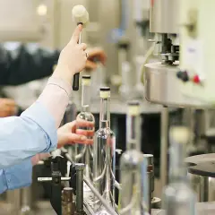 Pracownik na linii produkcyjnej zamyka butelki, przygotowując je do dalszego etapu, gdzie sprawdzane jest, ile spirytus ma procent.