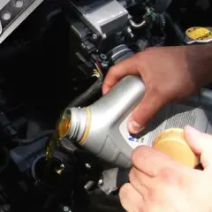 Mano che versa olio motore nel vano del motore. Il tappo giallo indica dove si mette l'olio motore.