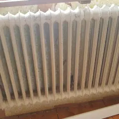 Gammal vit element med blommig tapet bakom. Kanske dags att ta bort elementet och tapeten för en renovering.