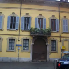 Facciata gialla del **Palazzo Belgioioso** con finestre dalle persiane azzurre e un balcone fiorito.