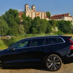Czarne Volvo V60 na tle malowniczego klasztoru i rzeki. Idealne na wakacyjne podróże, gdzie niskie volvo v60 spalanie pozwoli cieszyć się widokami.