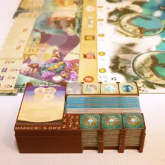 Spielkomponenten für das Dead Reckoning Brettspiel, darunter Karten, Marker und Würfel, sind ordentlich in braunen Halterungen gestapelt.