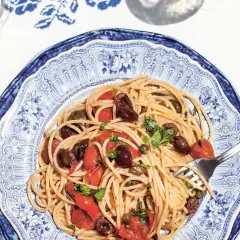 Spaghetti Puttanesca mit Oliven, Kapern und Tomaten auf einem blau-weißen Teller.