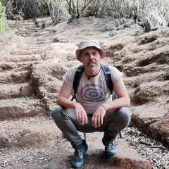 Hombre con sombrero y mochila en el sendero de los sentidos Tenerife, rodeado de vegetación y escalones de tierra.