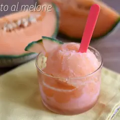 Sorbetto al melone rinfrescante in un bicchiere, con fette di melone fresco sullo sfondo.