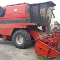 Czerwona maszyna rolnicza Bizon BS Z110 z hederem, gotowa do pracy na polu.