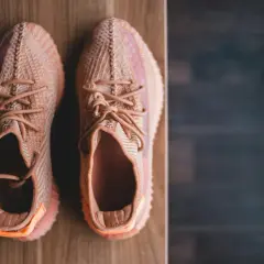 Pomarańczowe sneakersy z plecionki, idealne na szeroką stopę, leżą na drewnianym blacie.
