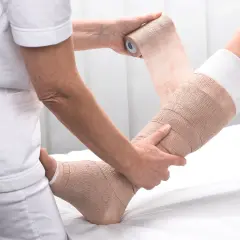 Eine Person wickelt einen Verband um ein Bein zur Kompression.