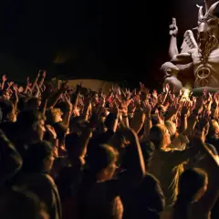 Tłum ludzi z podniesionymi rękami przed posągiem przypominającym baal demona.