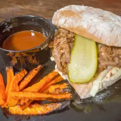 Pulled pork-macka med krispiga sötpotatispommes och en skål med smakrik sås till pulled pork.