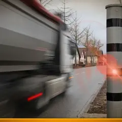 Ein Lkw rast an einem Blitzer vorbei. Der Blitz leuchtet auf, als der Fahrer zu schnell fährt.