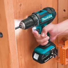 Une perceuse Makita d'origine, tenue par une main, perce un trou dans du bois. L'outil est puissant et fiable.