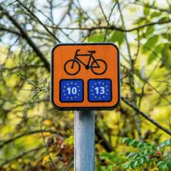 Pomarańczowy znak rowerowy z numerami 10 i 13, wskazujący drogę na trasie rowerowej Świnoujście Hel.