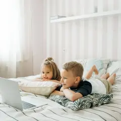 Dzieci leżą na łóżku, oglądając edukacyjne bajki dla dzieci na laptopie.