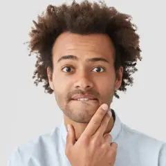 Uomo con capelli ricci e barba corta, con un dito sul mento, espressione pensierosa, come se avesse un sapore acido in bocca.