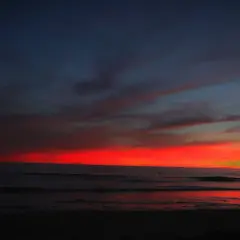 Kobieta w ciąży na tle zachodu słońca nad oceanem. Pamiętaj o ubezpieczeniu turystycznym w ciąży, by podróżować bezpiecznie.
