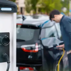 Mężczyzna ładuje czarny samochód elektryczny przy stacji ładowania.