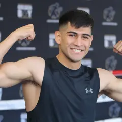 Alexis boxer flexes his biceps, smiling confidently in a black tank top.